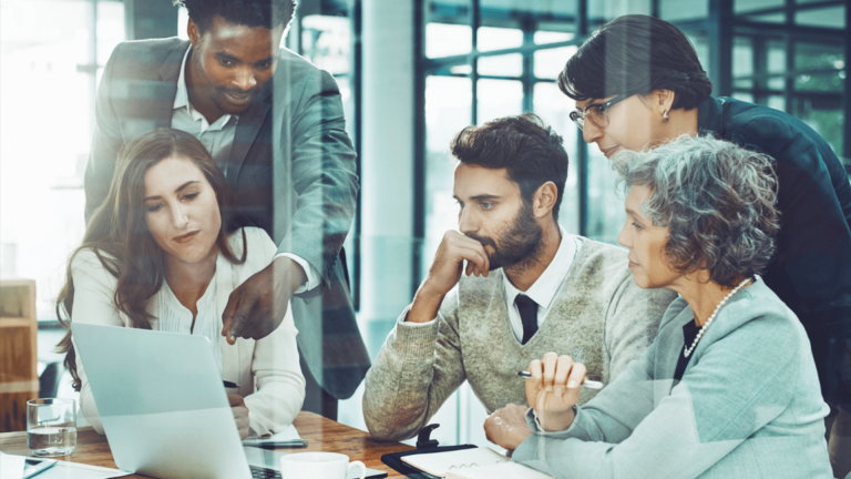 five people convene in an office, viewing a laptop together